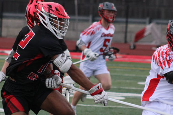 Lacrosse players in action on a field with red and black uniforms.